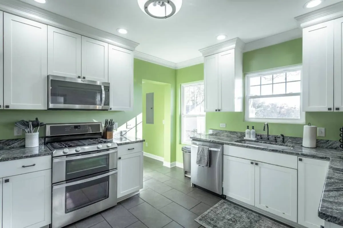 A modern kitchen featuring stainless steel appliances, a vibrant green accent wall, and spacious granite countertops. The kitchen is bright and cheerful, with plenty of room for cooking and gathering. The setting hints at both the excitement of preparing meals and the enjoyment of hosting family or friends.