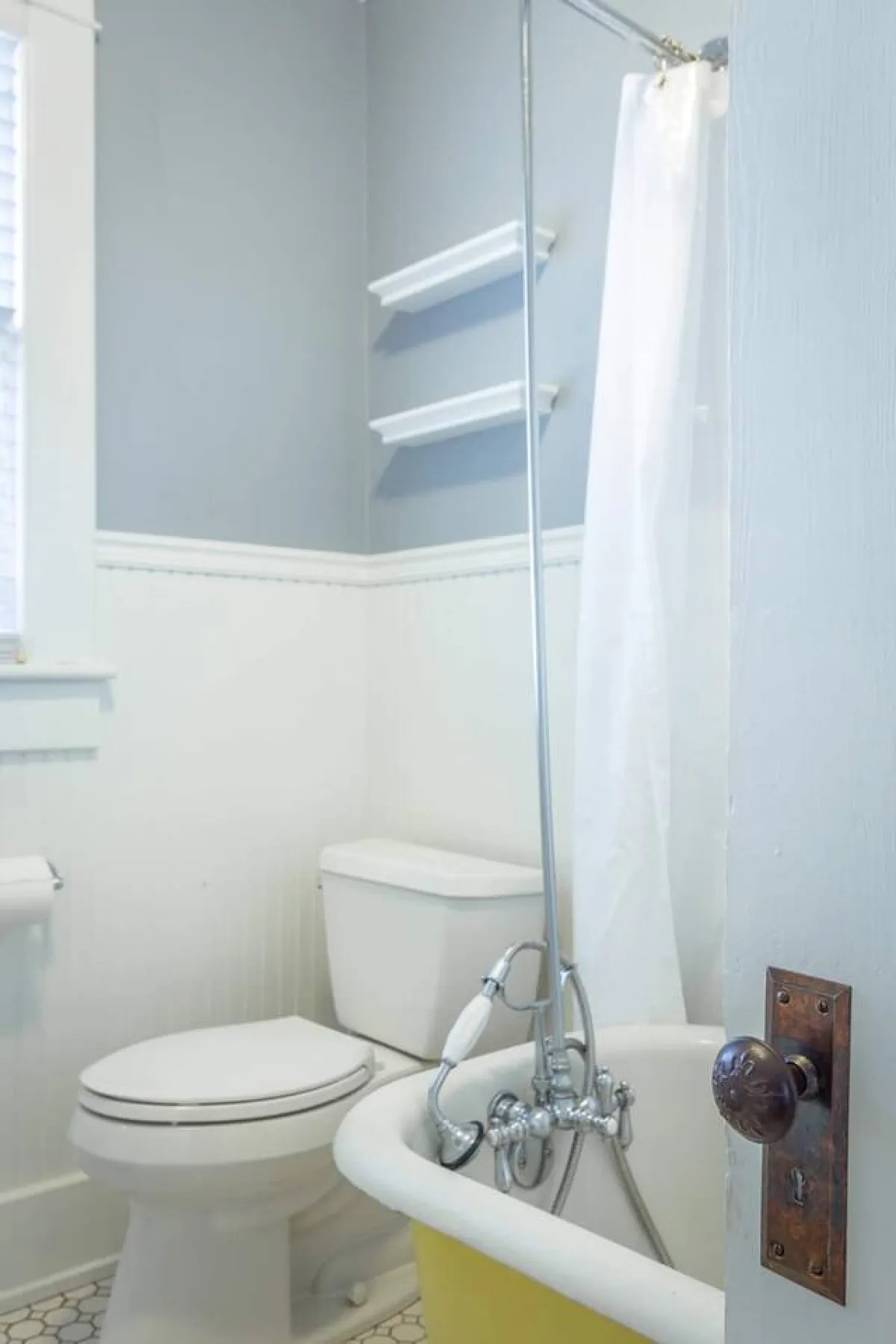 A bright, tranquil bathroom featuring a clean bathtub, modern toilet, and wall shelves with essentials. The inviting shower curtain and thoughtful details create a spa-like environment for relaxation and self-care.