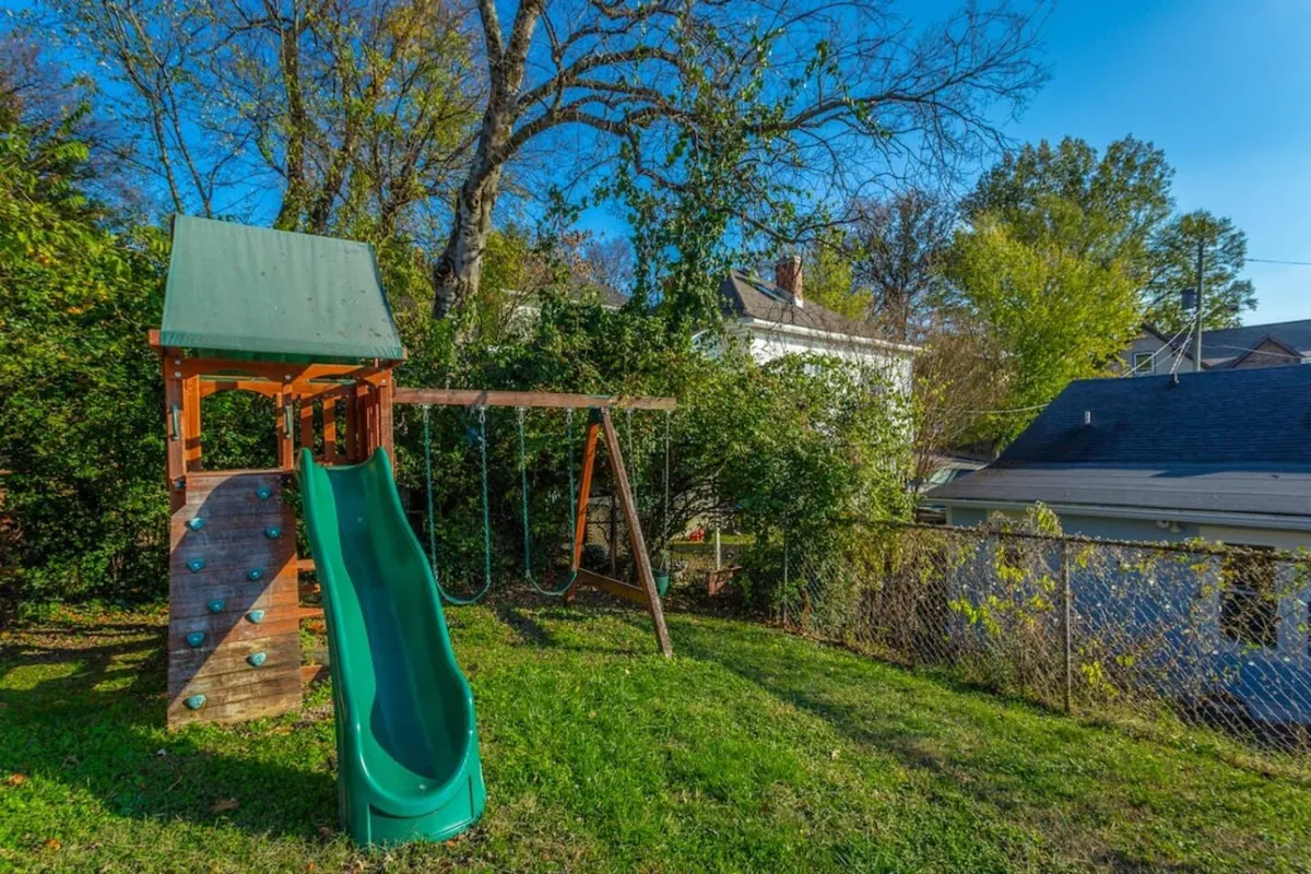 A vibrant playground scene with a slide and swings, surrounded by green space, where children are actively playing and families gather for outdoor fun or picnics.