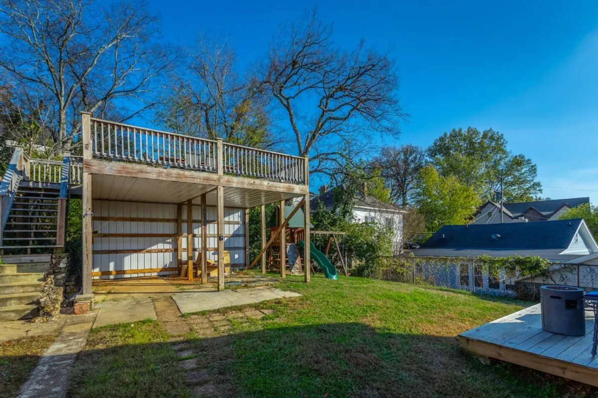 An inviting backyard scene with an elevated deck, a playset featuring a slide, and a spacious grassy area. The image suggests a relaxed, fun atmosphere ideal for group gatherings or winding down after a night out, with the potential for a cozy evening by the fire pit under open skies.