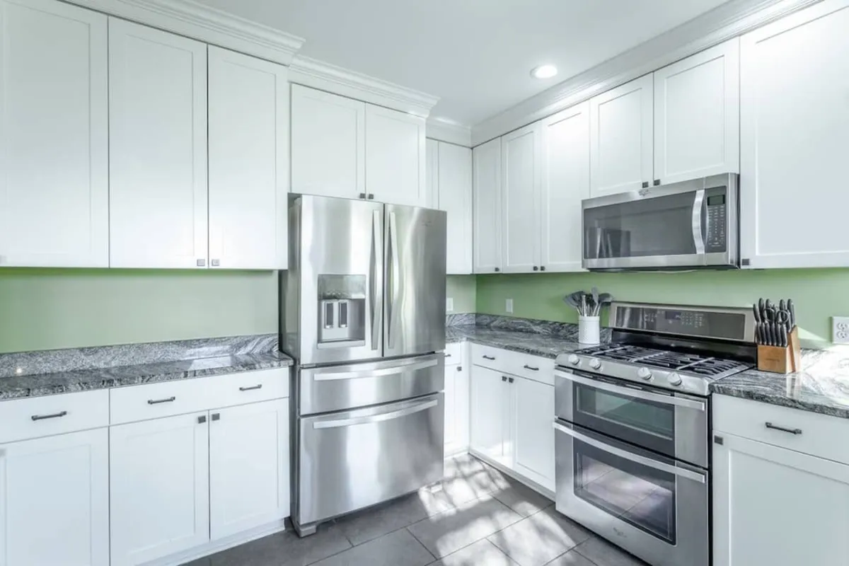 A welcoming kitchen scene with a stainless steel refrigerator, granite countertops, white cabinetry, and prominent kitchen appliances. The layout is functional yet inviting, ideal for meal prep, cooking, and socializing with loved ones.