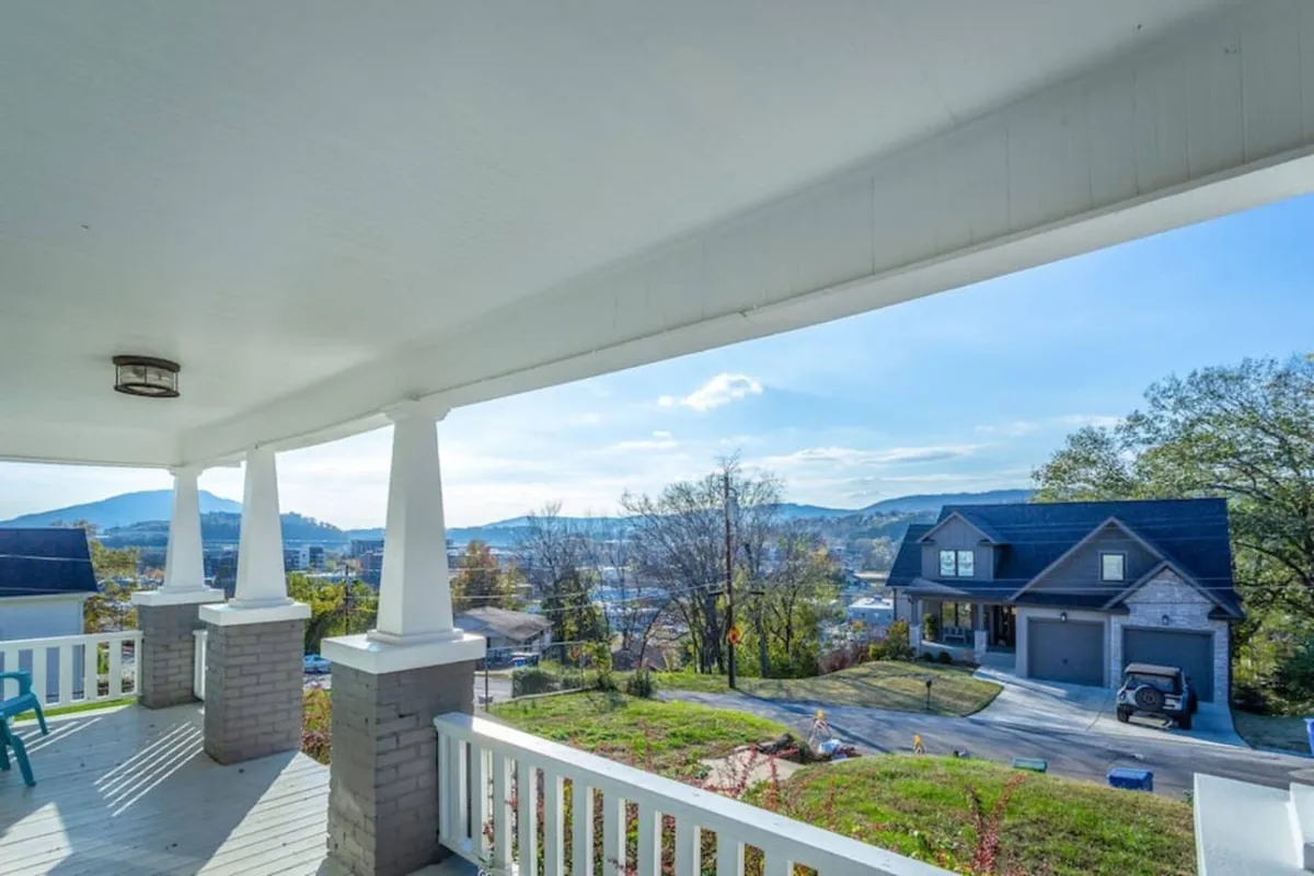The exterior of a charming single-family house with classic porch columns, offering a sweeping view of the Tennessee mountains. The porch is an inviting space for guests to relax, watch sunsets, and enjoy the peaceful, upscale neighborhood setting. Neighboring homes enhance the sense of community, while the natural backdrop creates a serene atmosphere.