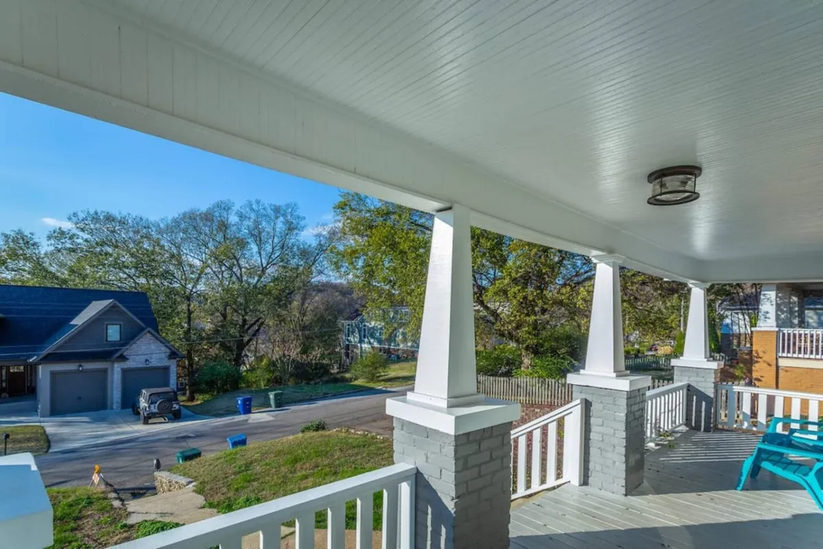 A charming exterior porch with bright blue chairs and columns, set against a backdrop of a welcoming neighborhood view. The scene is cheerful and inviting, capturing the spirit of relaxing or gathering outside before or after an evening out.