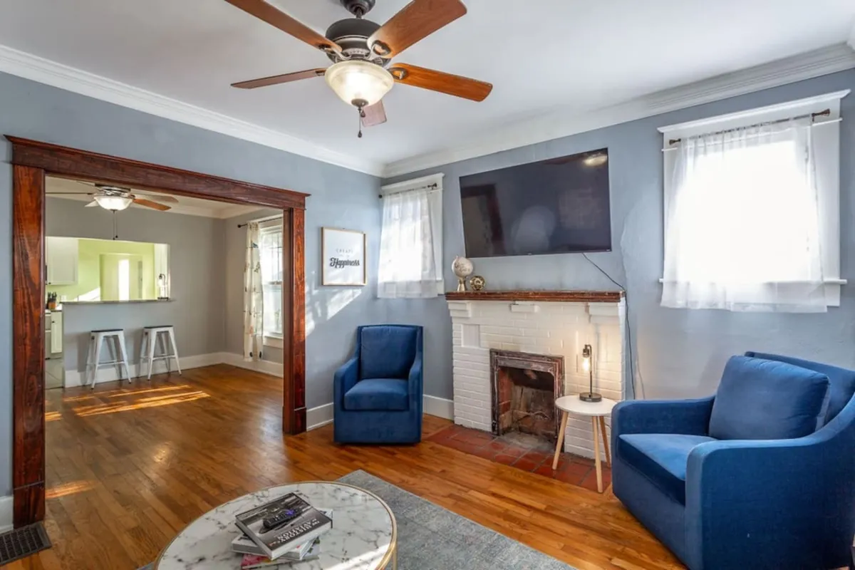 A cozy living room scene centered around blue armchairs, a fireplace, a television, and wooden accents. The warm, sunlit space is perfect for gathering, socializing, and enjoying intimate moments or movie nights.