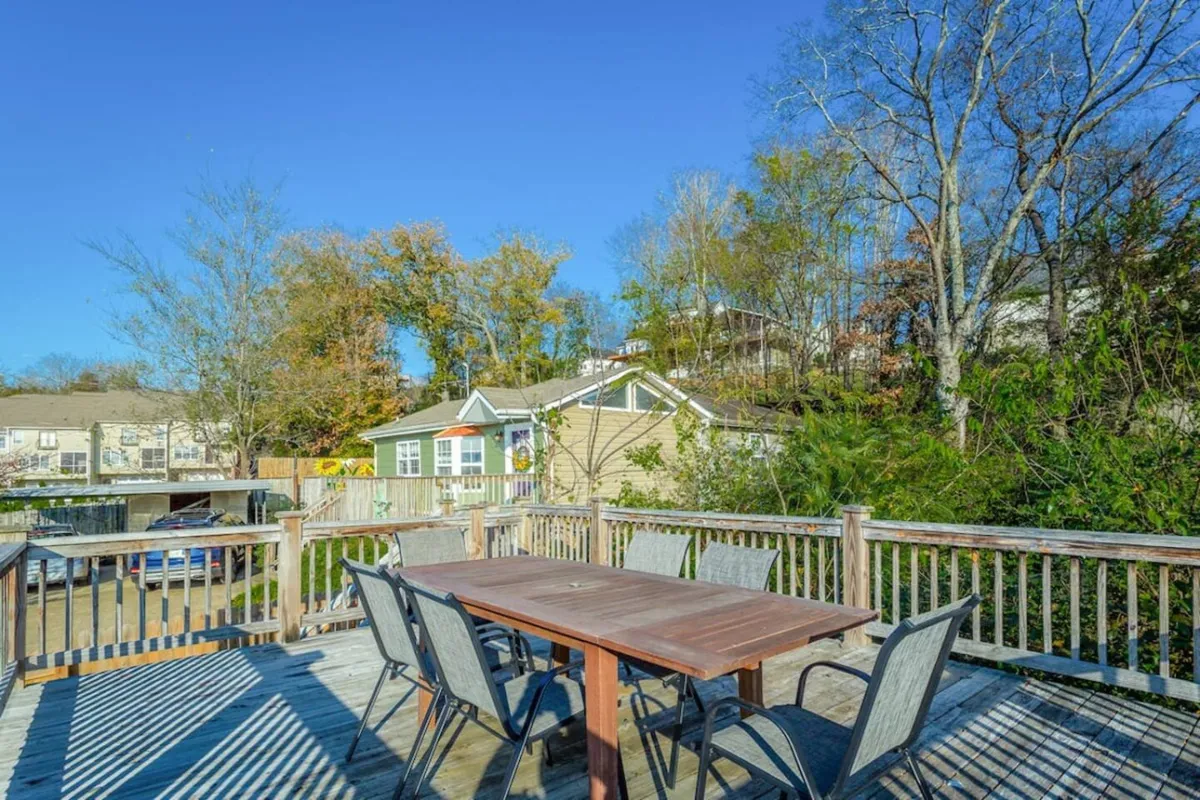 A spacious wooden deck surrounded by lush trees, featuring a large outdoor dining table. The setting is relaxed and ideal for family gatherings, group celebrations, and enjoying the beauty of nature from a central spot.